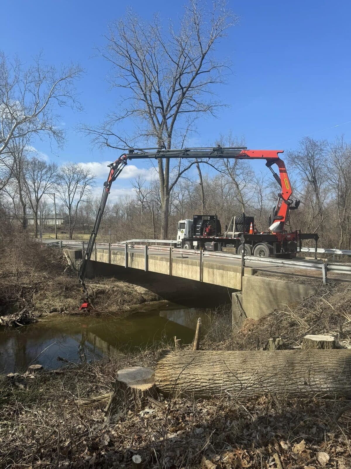 Truck-mounted hydraulic boom removing a limb over a creek